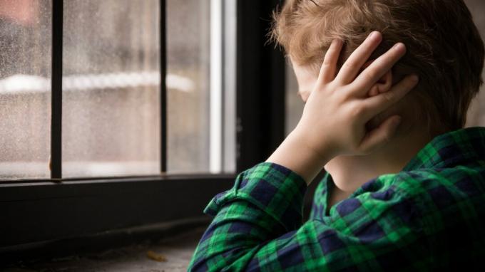Kisfiú állt az ablak mögött, szomorú hangulatban. Szomorú tinédzser az ablakon néz, és kezével bezárja a fülét. Boldogtalan gyermek egy kockás inget. Egyedül otthon. Szomorú.