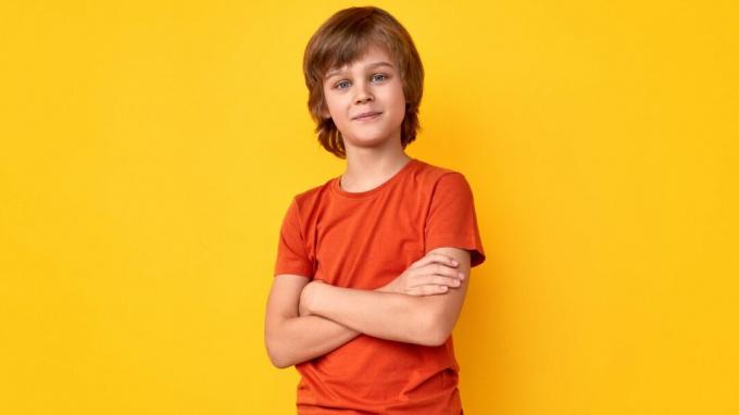 Pozitív preteen fiú alkalmi ruhában, keresztbe fektetve, és élénk sárga háttérrel nézi a kamerát